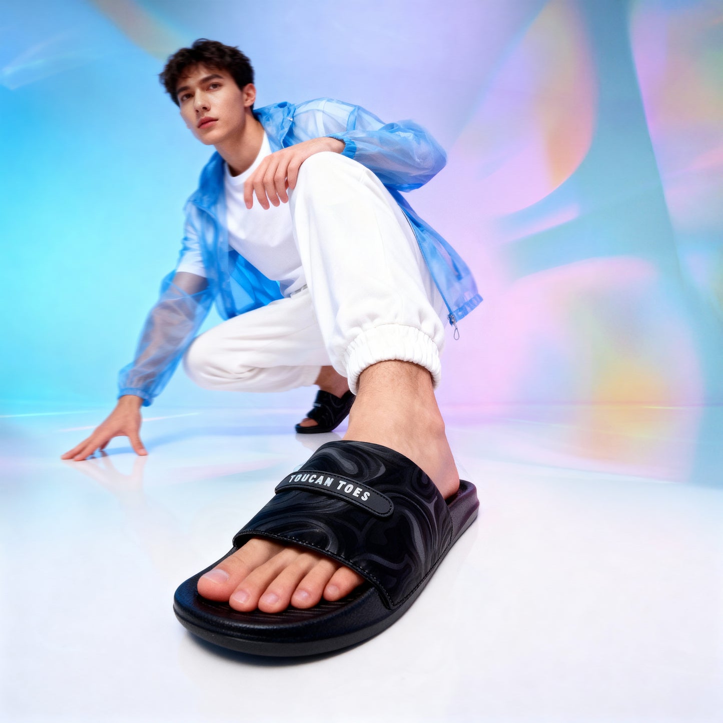 Man wearing Toucantoes black slides with white joggers on colorful studio background