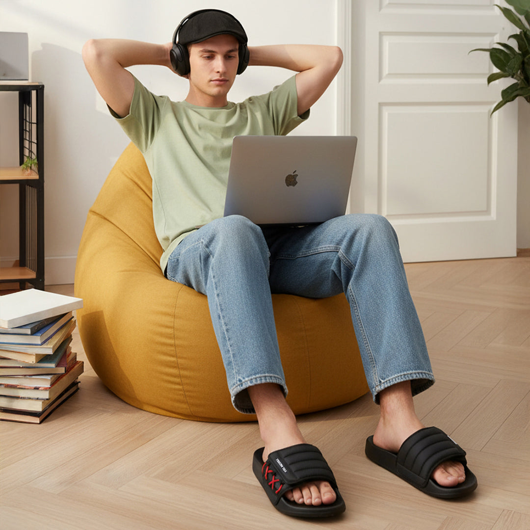 Man relaxing on yellow bean bag wearing black Toucantoes slides, casual indoor setting