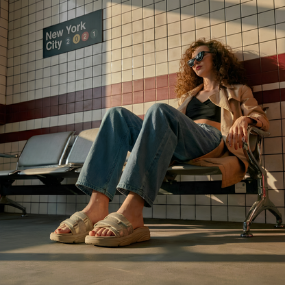 Woman wearing stylish beige sandals from Toucan Toes, sitting in New York subway station
