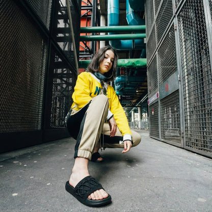 Woman in yellow sweatshirt and joggers wearing black Toucan Toes slides, urban setting